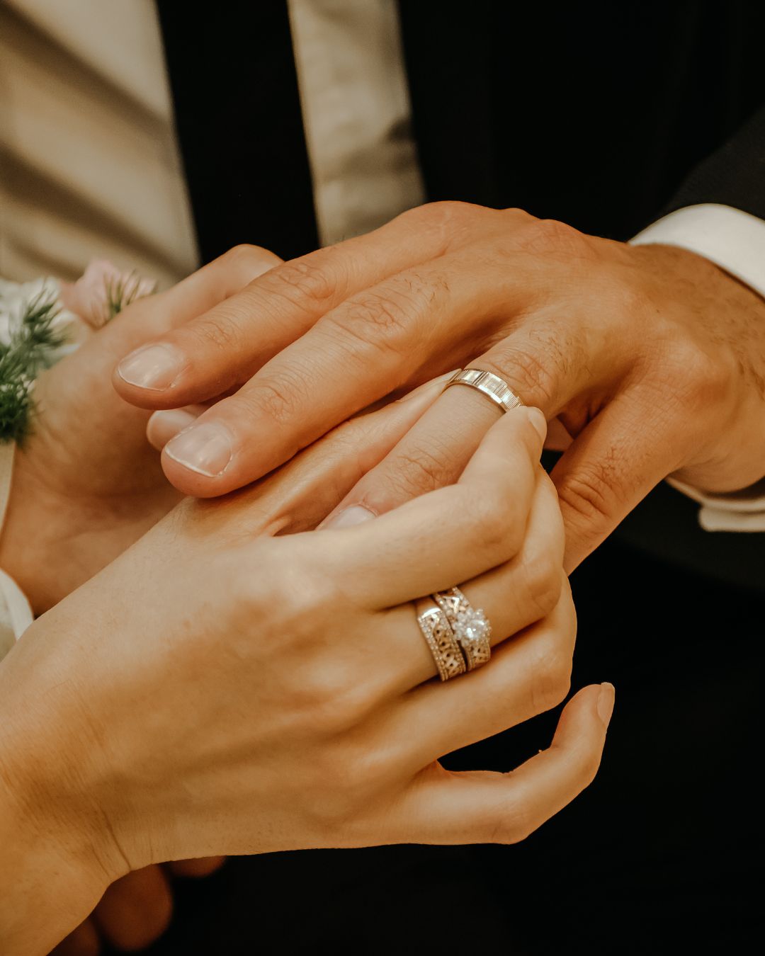 Mani che si scambiano fedi nuziali durante un matrimonio, simbolo di unione e promessa. Anelli in oro bianco e diamanti di Atelier Diamanti