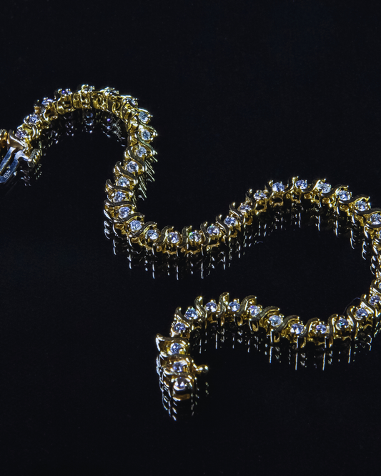 Elegante bracciale tennis in oro giallo con una fila continua di diamanti scintillanti, posizionato su una superficie scura riflettente. Gioiello di lusso e raffinatezza di Atelier Diamanti, ideale per ogni donna a Roma.