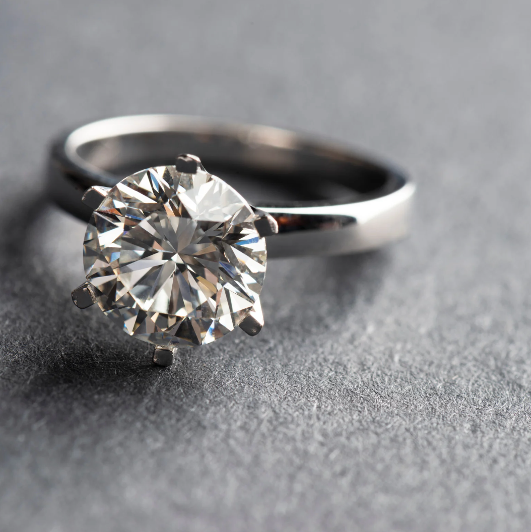 anello di fidanzamento con diamante rotondo centrale e montatura in oro bianco con sei griffes, classico modello tiffany, appoggiato su un lato