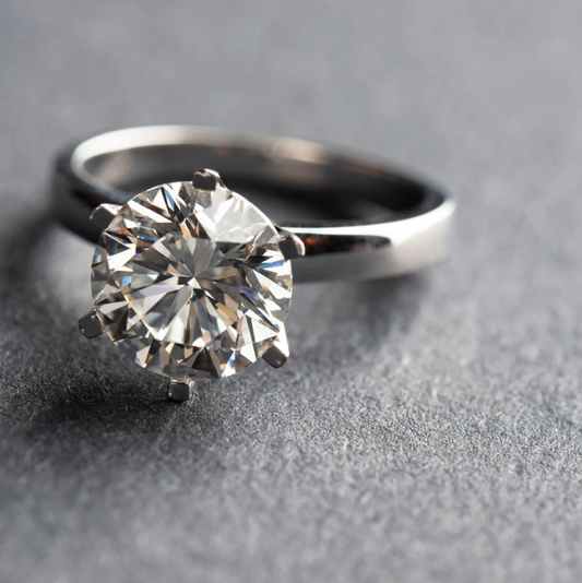 anello di fidanzamento con diamante rotondo centrale e montatura in oro bianco con sei griffes, classico modello tiffany, appoggiato su un lato