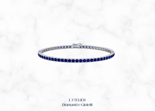 Bracciale modello tennis in oro bianco o platino con zaffiri blu e altre pietre preziose, su sfondo scuro. Gioiello di lusso Atelier Diamanti
